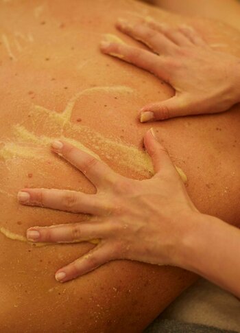 Hände massieren den Rücken einer Person mit einer Paste während der Udvarthana-Behandlung im Spa.