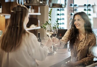 Zwei Frauen stoßen an der Hotelbar des Hotel Hochschober mit Wein und Cocktails an.