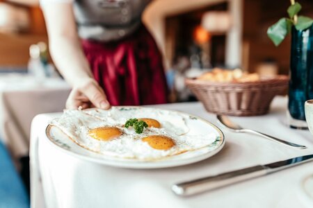 Eine Person serviert ein Frühstück mit Eiern auf einem gedeckten Tisch im Hotelrestaurant.