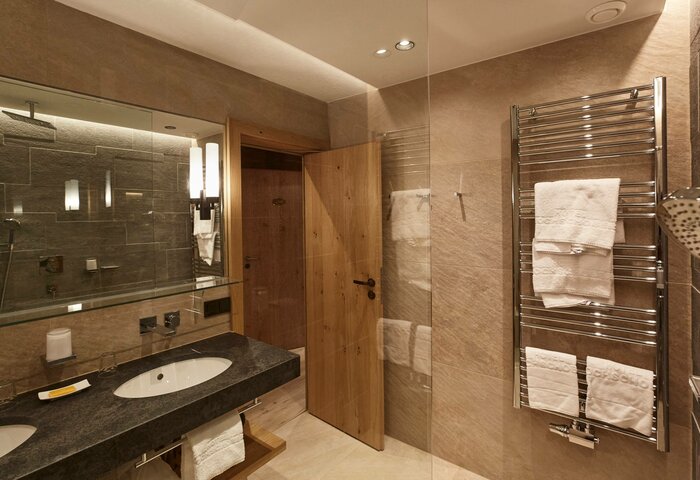 Family apartment studio bathroom at Hotel Hochschober A bathroom in the family apartment studio with a vanity, towel warmer, wooden door and stone surfaces.
