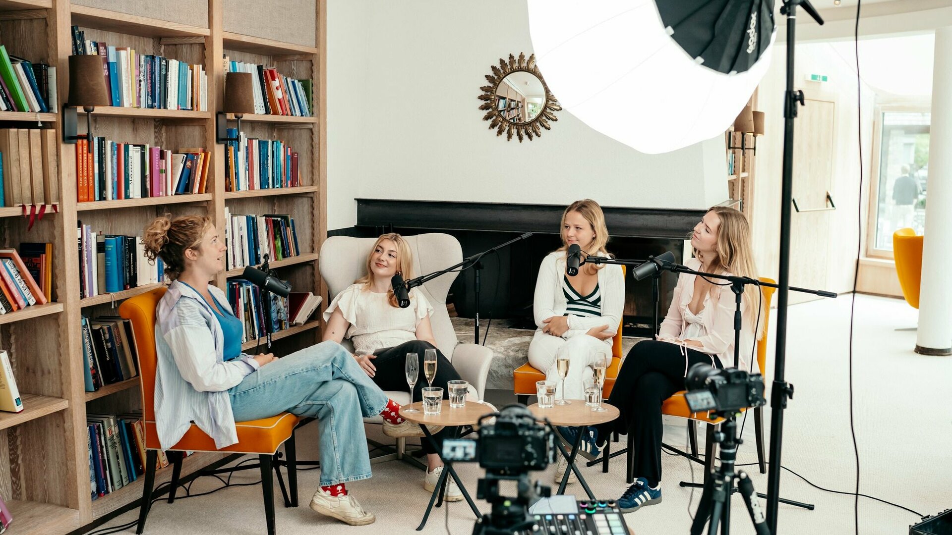 Four women record a podcast episode in a bright room with microphones and studio lighting.