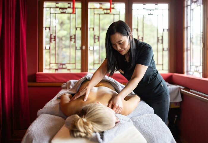 Eine Therapeutin massiert im Kristall Spa den Kopf und Rücken einer liegenden Frau auf einer Liege.