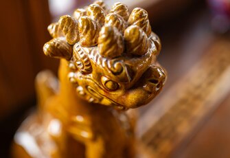 Eine goldene Drachenfigur ist nah aufgenommen und steht im warmen Licht auf einer Holzfläche.