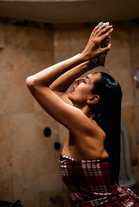 Eine Frau genießt eine Hamam-Dusche und hält den Wasserstrahl mit erhobenen Armen über dem Kopf.
