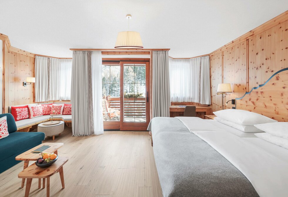 Helles Hotelzimmer mit Doppelbett, Sitzbereich und Balkon zum See.