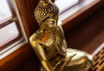 A golden Buddha figure sits on a wooden shelf by a window.