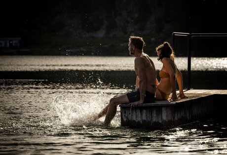Ein Mann und eine Frau sitzen auf einem Steg am beheizten See-Bad im Turracher See.