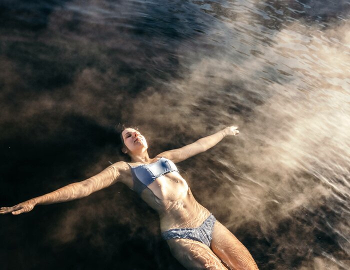 Wellness im Wasser: Frau in Bewegung Eine Frau liegt mit ausgebreiteten Armen im Wasser und wird von einer spritzenden Welle umgeben.