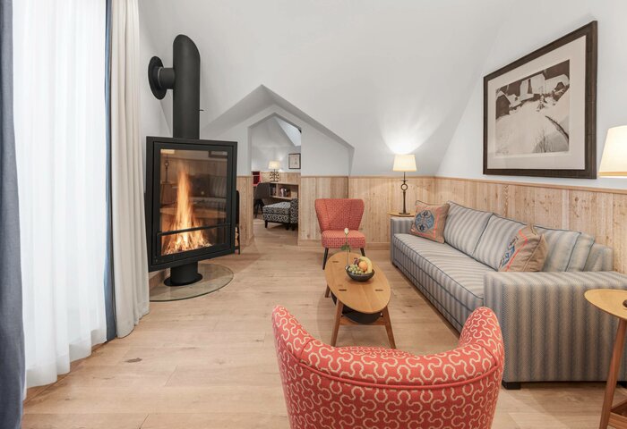 The Bergkristall family suite shows a living area with a fireplace, sofa, armchair and a view into the sleeping area.