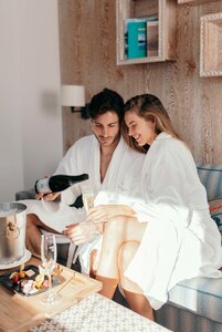 Ein Paar im Bademantel sitzt im Spa-Bereich und gießt Champagner in Gläser.