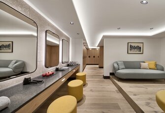 A bright relaxation room with mirrors, long counters, yellow stools and a sofa on a raised platform.