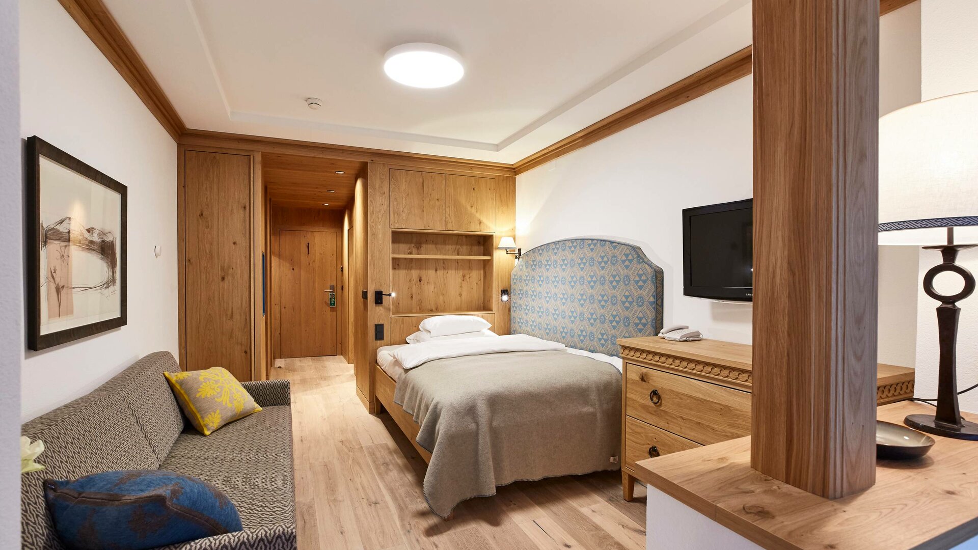 A single room with a bed, sofa, wood paneling and desk in Hotel Hochschober.