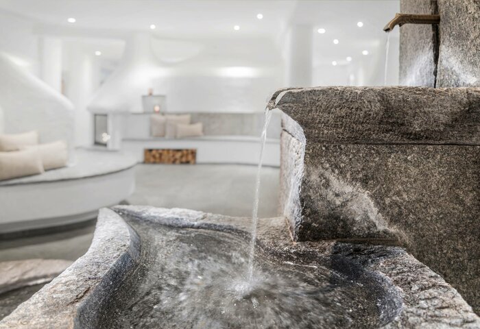 Ein steinerner Innenbrunnen lässt Wasser in ein flaches Becken im hellen Kristall Spa des Hotel Hochschober fließen.
