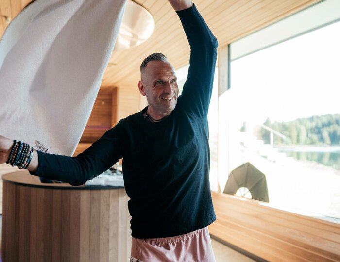 Ein Mann schwenkt ein großes Tuch in der Sauna und bereitet einen Aufguss vor.