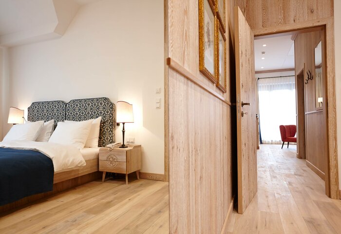 Bergkristall family suite at Hotel Hochschober A bedroom in the Bergkristall family suite with a double bed, bedside tables and a view into the bright hallway.
