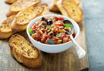 Eine Schale Antipasti mit geröstetem Brot auf einem Holzbrett.