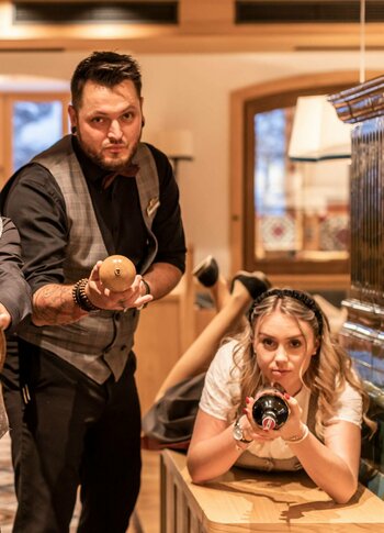 Hotelmitarbeiter im Restaurantbereich von Hotel Hochschober Vier Hotelmitarbeiter posieren im Restaurantbereich mit Tablett, Flasche und Kamera neben einem Kachelofen.
