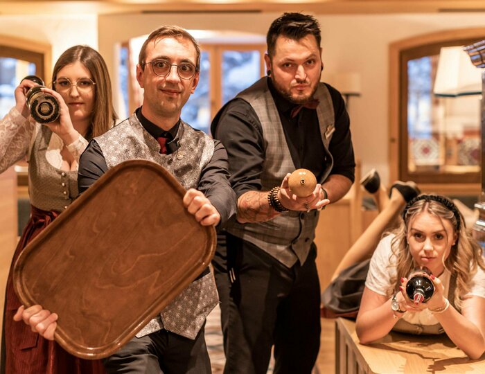 Hotel staff in the restaurant area at Hotel Hochschober Four hotel employees pose in the restaurant area with a tray, bottle and camera beside a tiled stove.