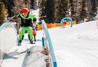 Ein Kind fährt auf Skiern über einen kleinen Parcours im Schnee.