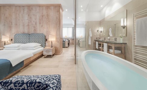 Ein Hotelzimmer mit Bett, Holzwand und freistehender Badewanne neben dem Badbereich.