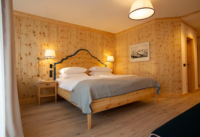 Superior pine room at Hotel Hochschober A wood-paneled superior pine room with a double bed, bedside tables, warm lighting and a light wood floor.