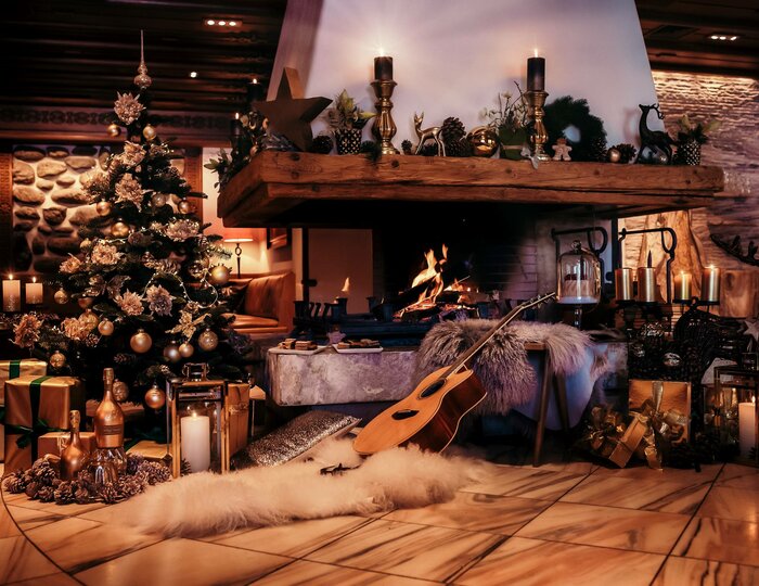 Ein geschmückter Christbaum und ein brennender Kamin prägen die festliche Bergweihnachtszene.