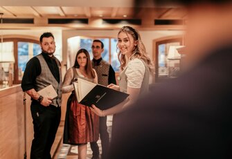 Vier Mitarbeiter stehen an der Hotelrezeption, während eine Frau lächelnd eine Mappe hält.