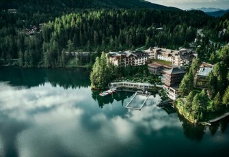 Der Blick von oben zeigt das Hotel Hochschober direkt am See, umgeben von Wald und Bergen.