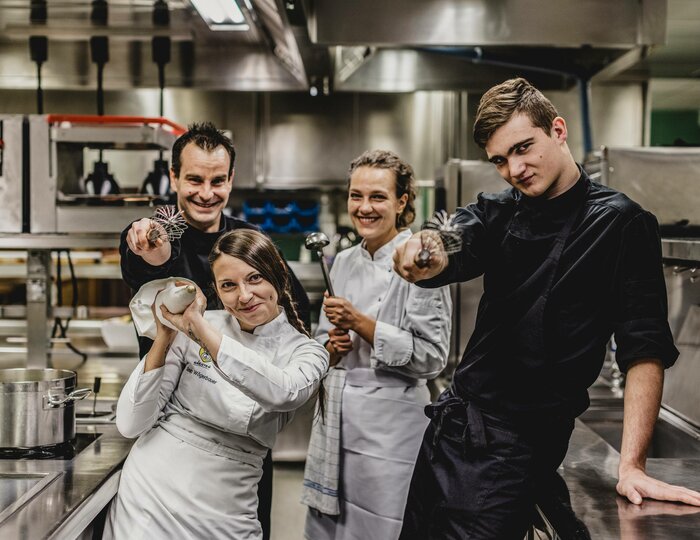 Four kitchen team members stand in the hotel kitchen and look at the camera.