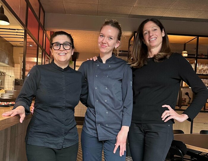 Drei Mitarbeiterinnen stehen im Hotelrestaurant nebeneinander und lächeln in die Kamera.
