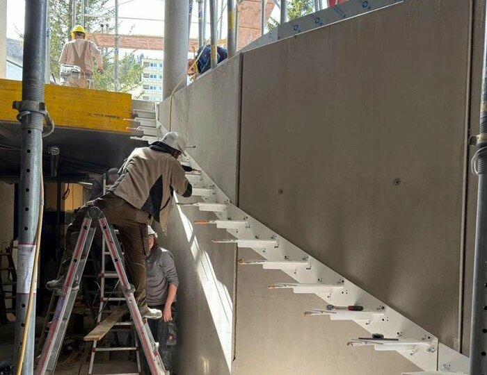 Umbau Hotel Hochschober: Treppenbau in Bauwoche 6 Handwerker montieren eine Treppe auf der Baustelle im Hotel Hochschober, umgeben von Werkzeugen und Baugeräten.