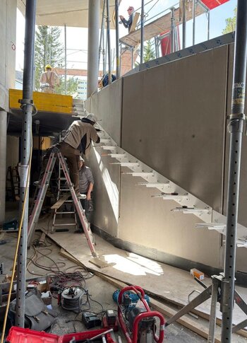Umbau Hotel Hochschober: Treppenbau in Bauwoche 6 Handwerker montieren eine Treppe auf der Baustelle im Hotel Hochschober, umgeben von Werkzeugen und Baugeräten.