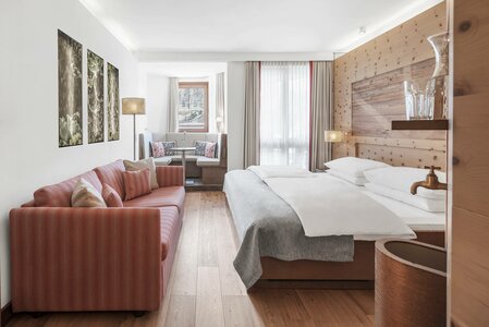 A bright hotel room with a double bed, pink sofa and window seating nook at Hotel Hochschober.