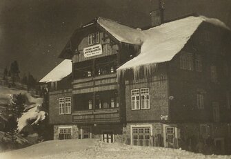 A snow-covered historic hotel building with balconies and an old wooden sign stands at night.