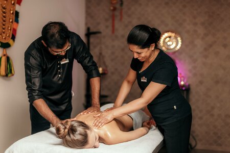 Eine Frau erhält eine Rückenmassage, während zwei Spa-Mitarbeitende sie auf einer Liege behandeln.