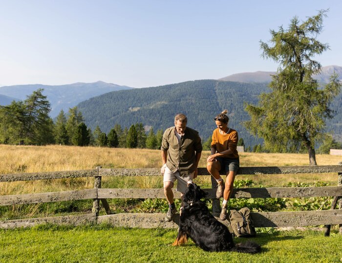 Ein Paar mit Hund sitzt auf einem Weidezaun nach dem Wandern.