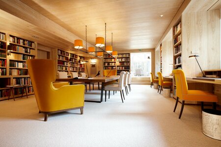 Eine helle Hotelbibliothek mit Bücherregalen, Lesetischen und gelben Sesseln.