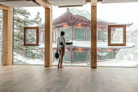 Eine Frau steht in einem hellen Raum vor einer großen Fensterfront und blickt auf den verschneiten Chinaturm.