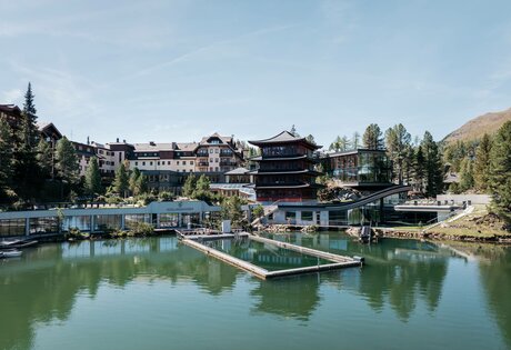 Der Chinaturm und das See-Bad des Hotel Hochschober liegen am Ufer des Sees mit Stegen und Gebäuden im Hintergrund.