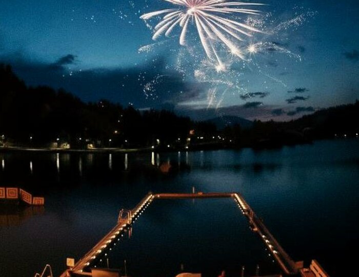 Silvesterfeuerwerk am See beim Hotel Hochschober Feuerwerk über dem See bei Nacht mit beleuchteter Badeplattform im Vordergrund.