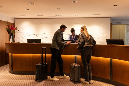 Zwei Gäste stehen an der Rezeption des Hotel Hochschober und sprechen mit dem Empfangspersonal.