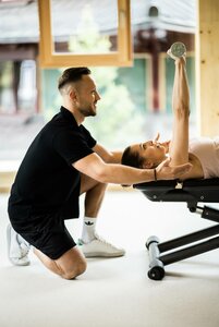 Ein Trainer unterstützt eine Frau beim Yoga auf einer Liege im hellen Spa-Bereich.