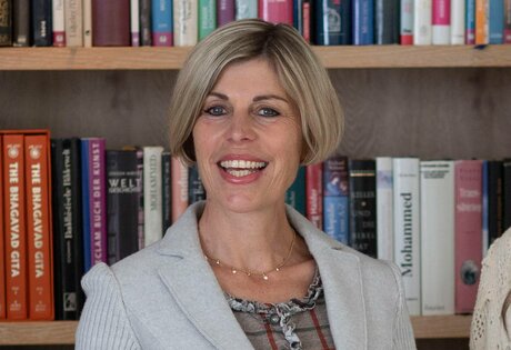 A smiling staff member stands in front of a bookshelf in the hotel library.