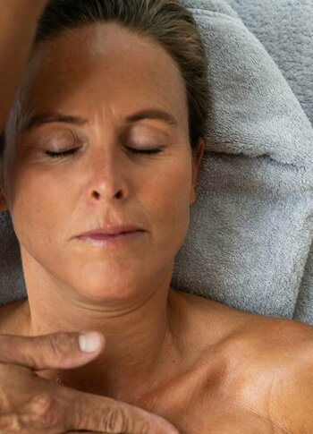 Eine Frau liegt mit geschlossen Augen auf einer Liege, während eine Massage im Kristall Spa durchgeführt wird.