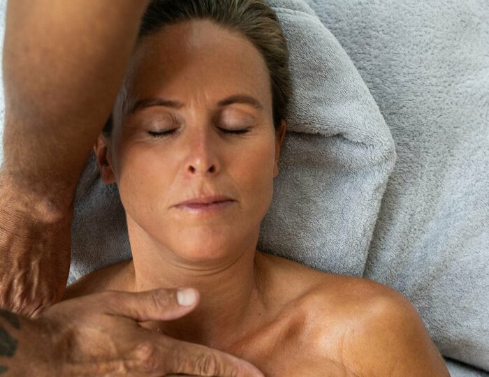 Haki Stretch & Relax Massage im Kristall Spa Eine Frau liegt mit geschlossen Augen auf einer Liege, während eine Massage im Kristall Spa durchgeführt wird.