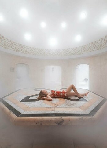Orientalischer Hamam im Hotel Hochschober Eine Person liegt entspannt auf der erhöhten Steinfläche im orientalischen Hamam, während dichter Dampf den Raum erfüllt.