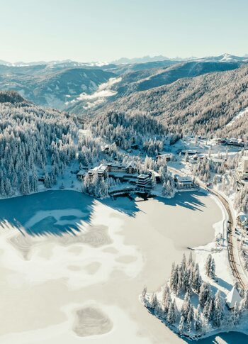 Winter aerial view of hotel on Turracher See Aerial view of Hotel Hochschober on the frozen Turracher See, surrounded by snowy slopes and forest.