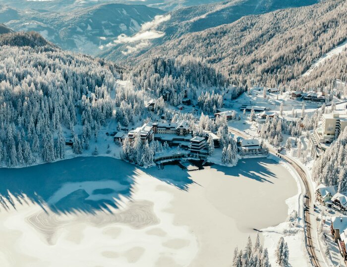 Winter aerial view of hotel on Turracher See Aerial view of Hotel Hochschober on the frozen Turracher See, surrounded by snowy slopes and forest.
