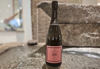 A bottle of Xanobis sparkling wine stands on a stone fountain indoors.