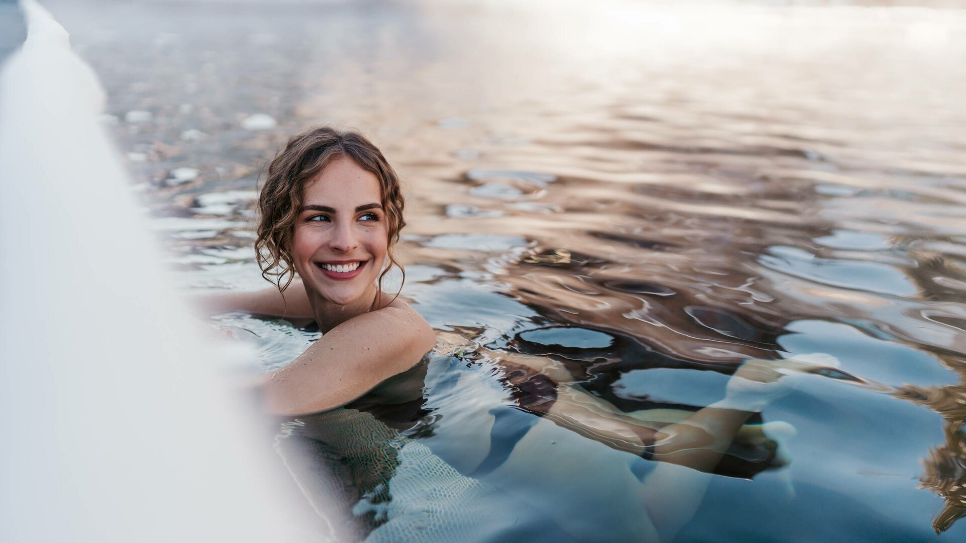 Eine Frau lächelt entspannt im beheizten See-Bad im Wasser.